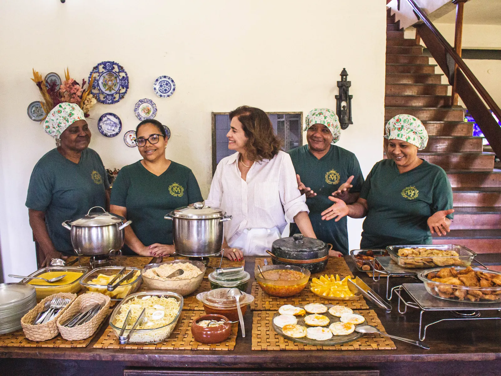 Equipe da cozinha do Hotel Fazenda Minas Real atrás da mesa do buffet, com panelas, ovos, queijo, salgados e doces