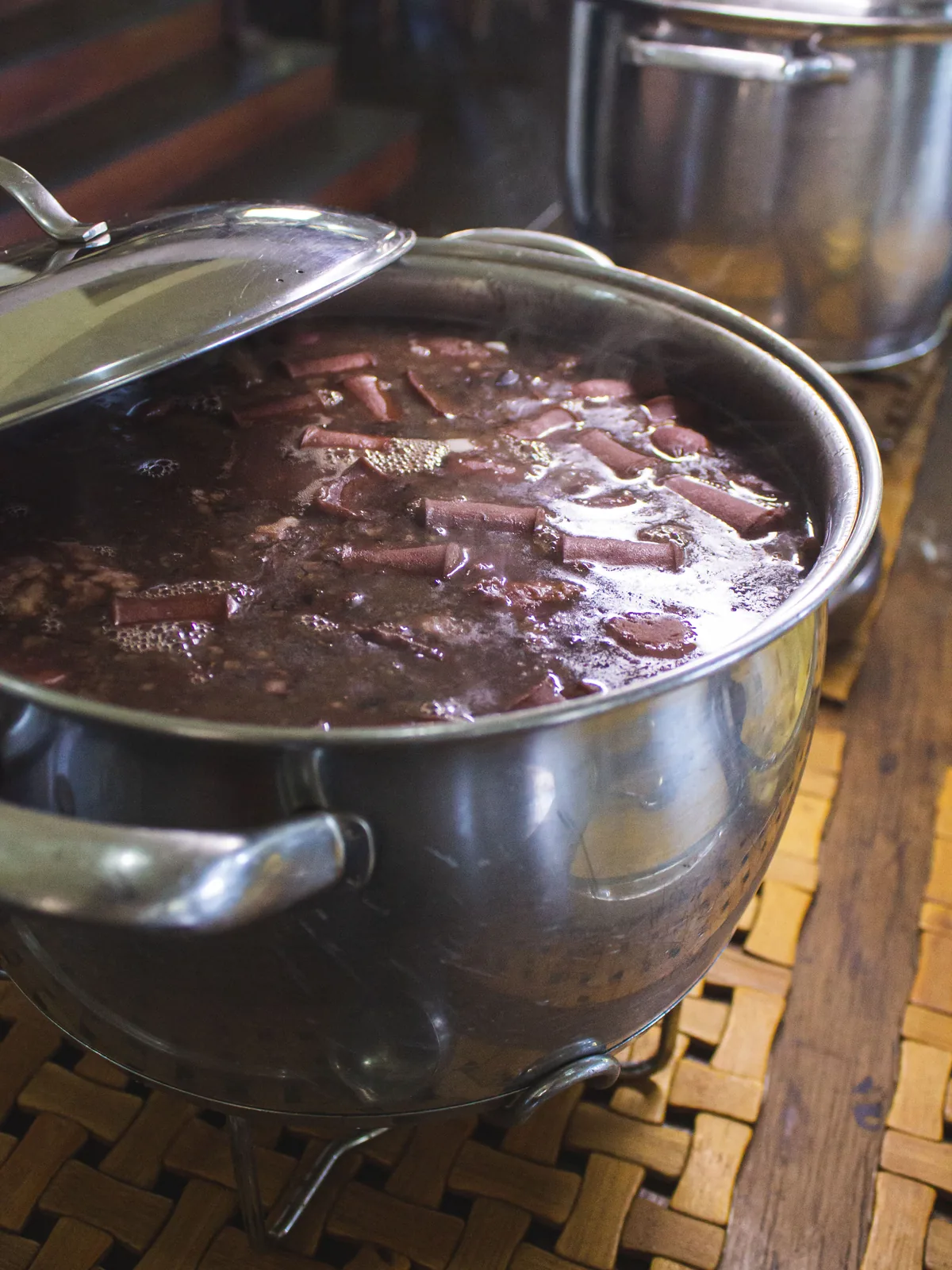 Panela de feijoada fumegando na cozinha do Hotel Fazenda Minas Real, com a tampa encostada e outra panela ao fundo