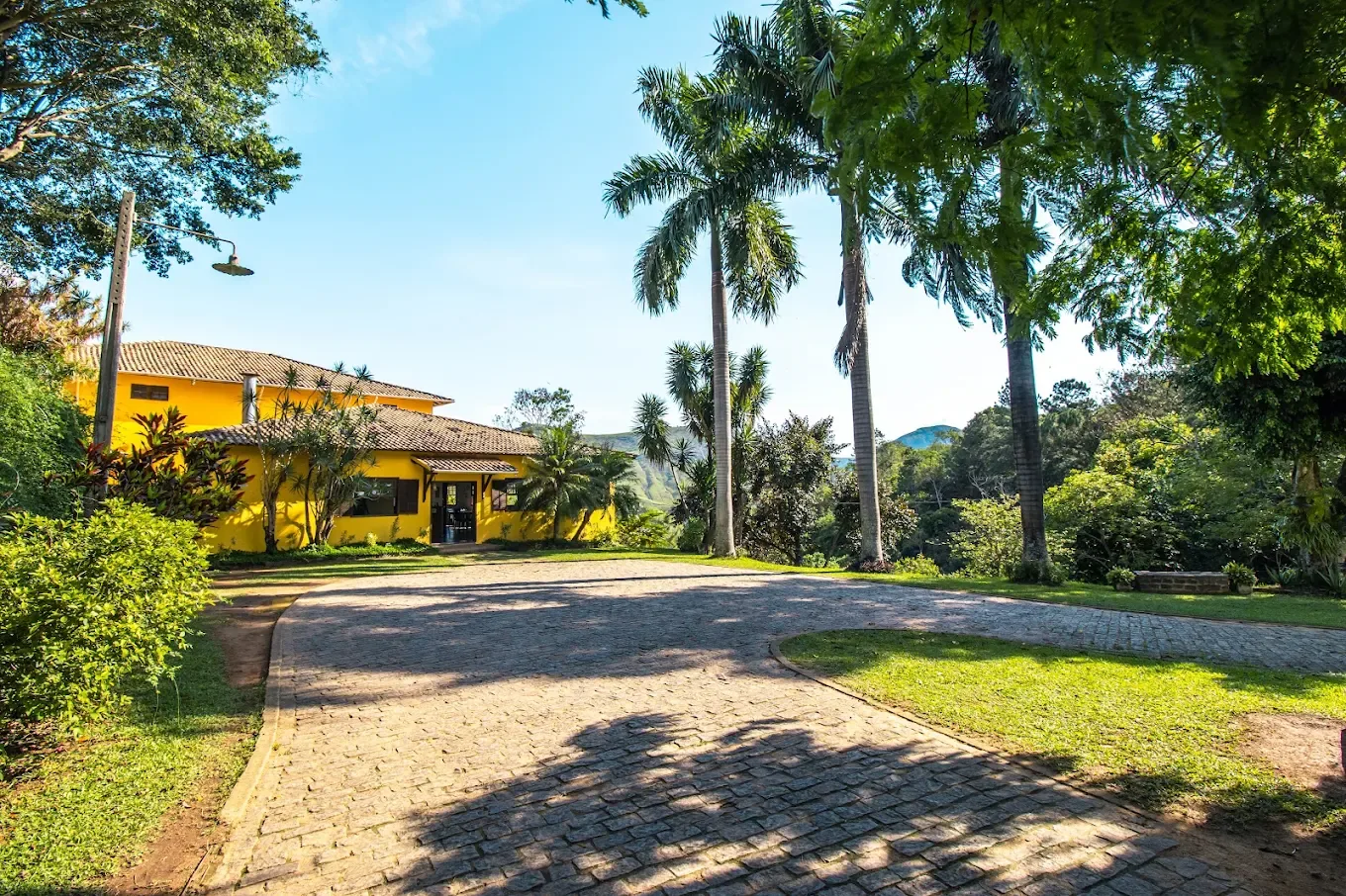 A entrada do Hotel Fazenda Minas Real, com o caminho de pedra, as palmeiras e o morro ao fundo