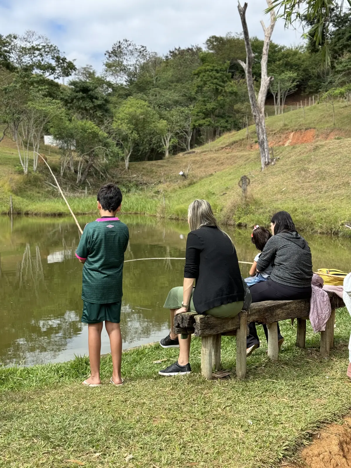 Hóspedes pescando na margem do lago do Hotel Fazenda Minas Real, com o vale e a mata ao fundo